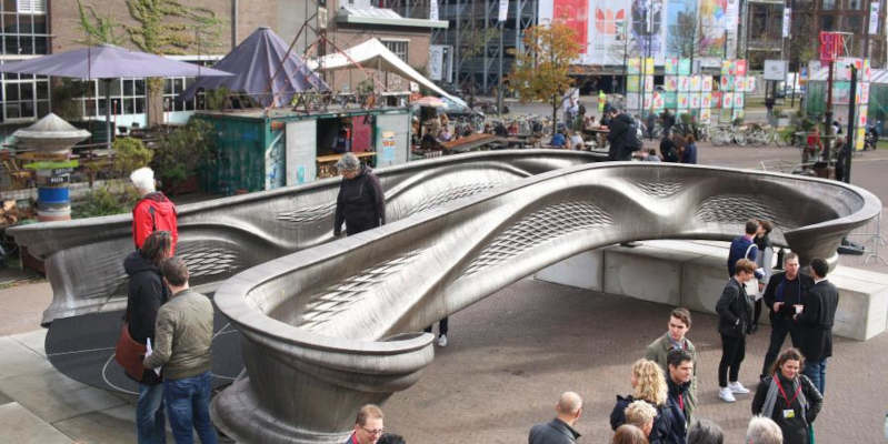 Pedestrians walk over MX3D's 3D printed bridge, whilst it is on display.