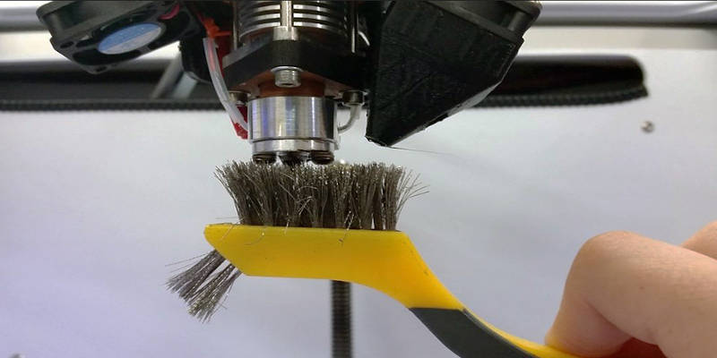 Brushing a 3D printer nozzle to clean it, using a wire brush